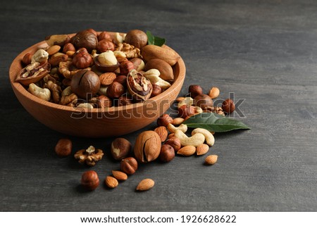 Wood bowl with different tasty nuts on gray wooden background