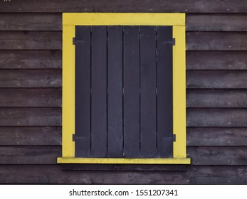 Wood Cabin Window With Storm Shutters In A Yellow Frame.