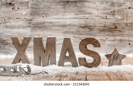 Wood Craft Rustic Christmas Background With Wooden Letters Spelling Xmas Standing In Snow With A Star And Small Kids Sleigh Or Toboggan Against A Weathered Wooden Wall With Copyspace For Your Greeting