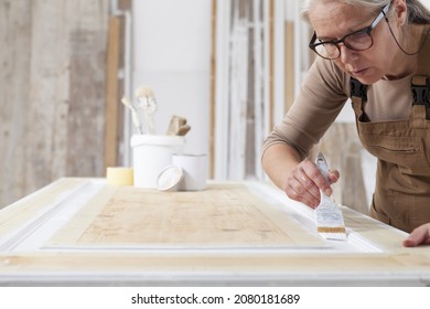 Wood Crafts, Woman Artisan Carpenter Painting With Brush And Paint Jar White The Door In Workshop, Wearing Overall And Eyeglasses, Interior Designer, Restoration, Diy And Handmade Works Concept