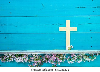 Wood Cross Hanging On Antique Rustic Wooden Background Over White And Pink Spring Flowers; Easter, Religious And Spiritual Background With Teal Blue Copy Space