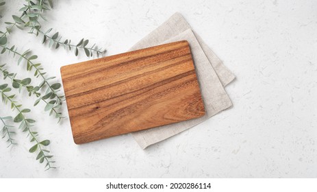 Wood cutting board with linen napkin and plant on marble table with copy space, top view