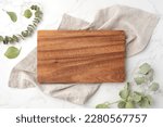 Wood cutting board on linen napkin with leaves on marble background, top view