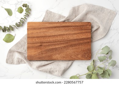 Wood cutting board on linen napkin with leaves on marble background, top view