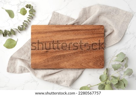 Wood cutting board on linen napkin with leaves on marble background, top view