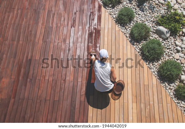 Wood deck renovation treatment, the\
person applying protective wood stain with a brush, overhead view\
of ipe hardwood decking restoration\
process