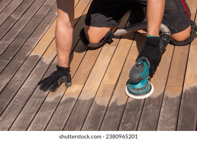Wood deck repair and maintenance, hands of deck cleaner sands and cleaning grey wooden surface with power sander tool