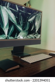 Wood Desk With Large Computer Monitor And White Mouse And Keyboard And Black Notebook With Soft Green Back Light