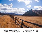 Wood fence along a road in a rural countryside landscape with mountains. Blue sky with clouds above.