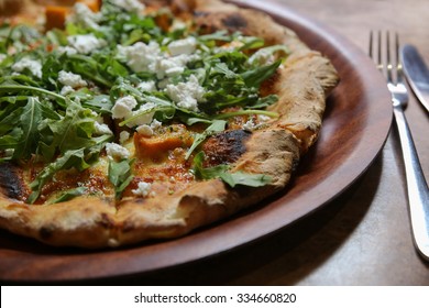 wood fired pumpkin feta rocket pizza on wooden plate, plant based diet, vegan, 