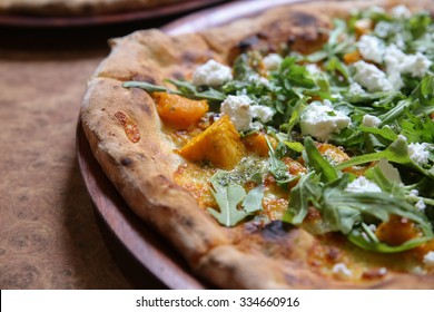 wood fired pumpkin feta rocket pizza on wooden plate, plant based, diet, vegan 