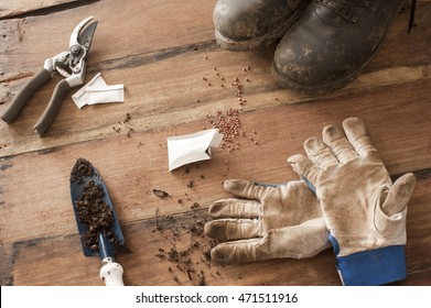 Wood Floor With Muddy Black Boots And Garden Sheers Next To Open Seed Packet And Gloves By Trowel With Dirt