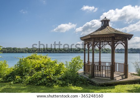A wood gazebo over looks the Niagara River in Niagara on the Lake, Ontario, Canada on a blue sky day. The United States can be seen in the distance.