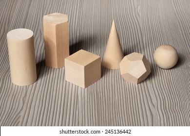 Wood Geometric Shapes On A Wood Surface. Cylinder, Prism, Cube, Cone, Polyhedron And Sphere.