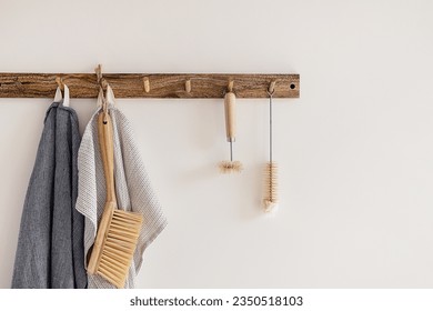 Wood hook rack with tea towels, broom and dish bottle brush hanging on a white wall on the modern style kitchen background. Smart organisation storage ideas. Eco friendly life. Natural materials. - Powered by Shutterstock