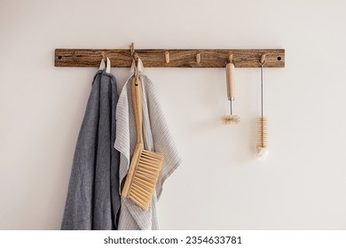 Wood hook rack with tea towels, broom and dish bottle brush hanging on a white wall on the modern style kitchen background. Smart organisation storage ideas. Eco friendly life. Natural materials. - Powered by Shutterstock