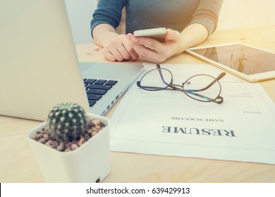 wood office table with human hand hold smartphone, tablet, cell phone with resume information, laptop and cactus flower on pot. concept of job search online. view form front office table. - Powered by Shutterstock