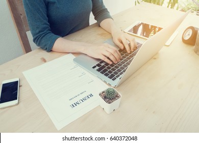 wood office table with young asian woman using laptop and resume information, tablet, cell phone, clock at home office. concept of job search online. view form front office table.