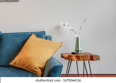 A Wood Plank End Table With A Vase And Flowers On Top. A Turquoise Couch Sits With A Yellow Pillow On Top.