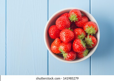 Wood planked blue breakfast table laid with Summer berry fruits and a stack of pancakes on an old wooden chopping board.  In the background, a bowl of oranges, glass of orange juice and white milk jug - Powered by Shutterstock