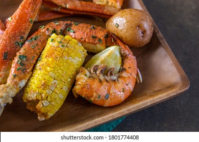 Wood Platter Of Southern Garlic Crabs Seafood Boil With Alaskan Crab Legs, Small New Red Potatoes, Corn On The Cob, And Shrimp With A Napkin