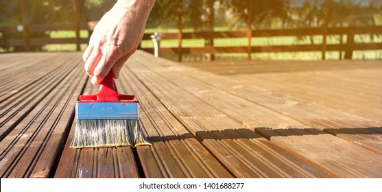 Wood protection against water and decay. The wooden terrace is painted. Paint brush in man's hand. Copy space - Shutterstock ID 1401688277