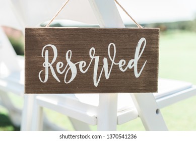 wood reserved seating sign hanging on white chairs outdoors