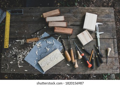 Wood Shavings And Vintage Woodworking Tools On A Professional Carpenter Workbench, Top View. Overhead Photo Of Woodworking Chisels Range And Wooden Stamp Design In Progress. Set Of Carpenter Tools.