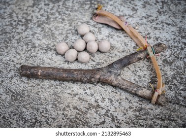 A wood slingshot with clay balls on the cement floor. A slingshot works like a small catapult, with rubber strips holding a stone or other projectile sits.