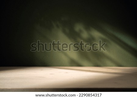 Wood table on dark green texture wall background. Composition with leaves shadow on the wall and light reflections. Mock up for presentation, branding products, cosmetics food or jewelry.