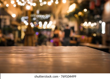 Wood table top with blur of lighting in night cafe restaurant (community) background/selective focus.