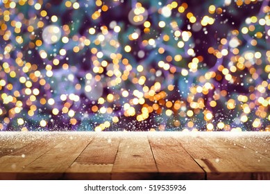 Wood table top with snow and decorative light bokeh on Christmas tree at night in background - can be used for display or montage your products