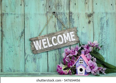 Wood Welcome Sign By Birdhouse And Purple Spring Flowers Hanging On Antique Rustic Mint Green Wooden Background; Springtime Background With Copy Space