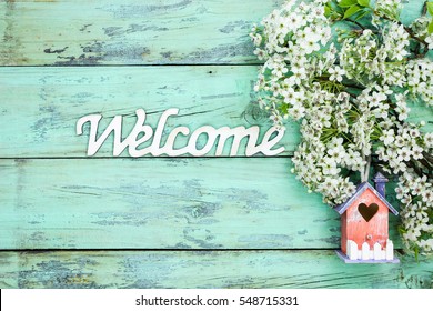 Wood Welcome Sign By Colorful Birdhouse And White And Pink Spring Flowers Hanging On Antique Rustic Mint Green Wooden Background; Springtime Background With Copy Space