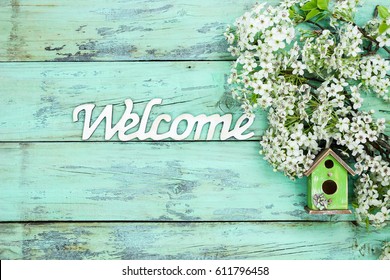 Wood Welcome Sign By Colorful Birdhouse And White And Pink Spring Flowers Hanging On Antique Rustic Mint Green Wooden Background; Springtime Background With Copy Space