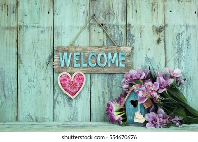 Wood Welcome Sign With Country Fabric Pink Heart By Teal Blue Birdhouse And Purple Spring Flowers Hanging On Antique Rustic Mint Green Wooden Background; Holiday Background With Painted  Copy Space