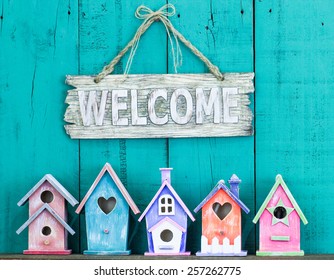 Wood welcome sign hanging over row of colorful spring birdhouses with antique teal blue rustic wooden background; purple, orange, pink, green  - Powered by Shutterstock