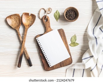 Wood white kitchen background with blank notebook for text, brown cutting board, cotton napkin and various spices. Copy space, top view