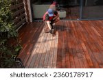 Wood worker applying nourishing deck oil with paintbrush on cleaned and sanded Ipe decking terrace boards
