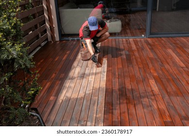 Wood worker applying nourishing deck oil with paintbrush on cleaned and sanded Ipe decking terrace boards - Shutterstock ID 2360178917