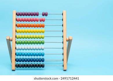 A wooden abacus with colorful beads on it. The beads are arranged in rows, with each row having a different color. The abacus is placed on a blue surface, and it is a simple and playful toy - Powered by Shutterstock