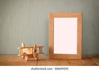 Wooden Airplane Toy Over Wood Table Next To Blank Photo Frame. Retro Filtered Image
