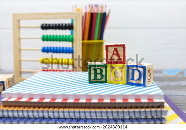 Wooden alphabet blocks on a white\
wooden background. Back to school, games for kindergarten,\
preschool education. Abacus, pencils, notebooks, blocks on the\
table.