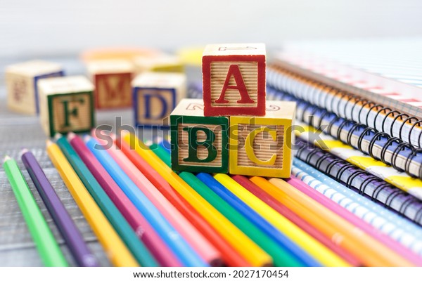 Wooden alphabet blocks on a white\
wooden background. Back to school, games for kindergarten,\
preschool education. Abacus, pencils, notebooks, blocks on the\
table.