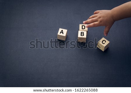Wooden alphabet cube with words ABCD closeup and children hands on black background. Selective focus and education concept
