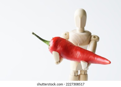 Wooden anthropomorphic mannequin with red pepper in his hands. copyspace. White background. Selective focus. Close-up