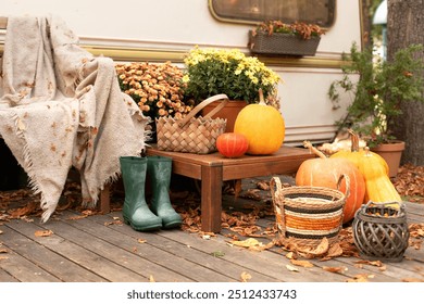 Wooden armchair with plaid near outside caravan trailer decorated for fall. RV house porch with garden furniture for relax nature. Interior cozy yard with rubber boots, flowers and pumpkins in garden. - Powered by Shutterstock