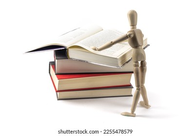 A wooden artist's mannequin standing at a pile of books, appearing to read an open book, isolated on white - Powered by Shutterstock