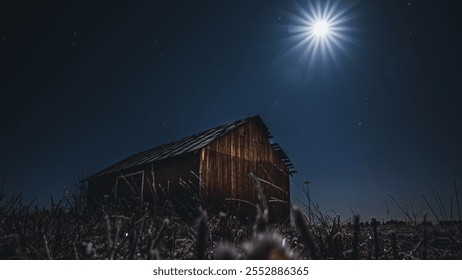 Wooden barn under a clear night sky with a bright moon, surrounded by frosted grasses. A peaceful rural landscape with moonlit scenery and deep blue sky - Powered by Shutterstock