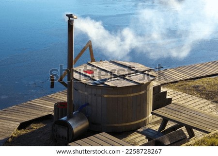 Wooden bathtub with a fireplace for burning wood and heating water, so the smoke comes out. Hot tub by the lake in winter.